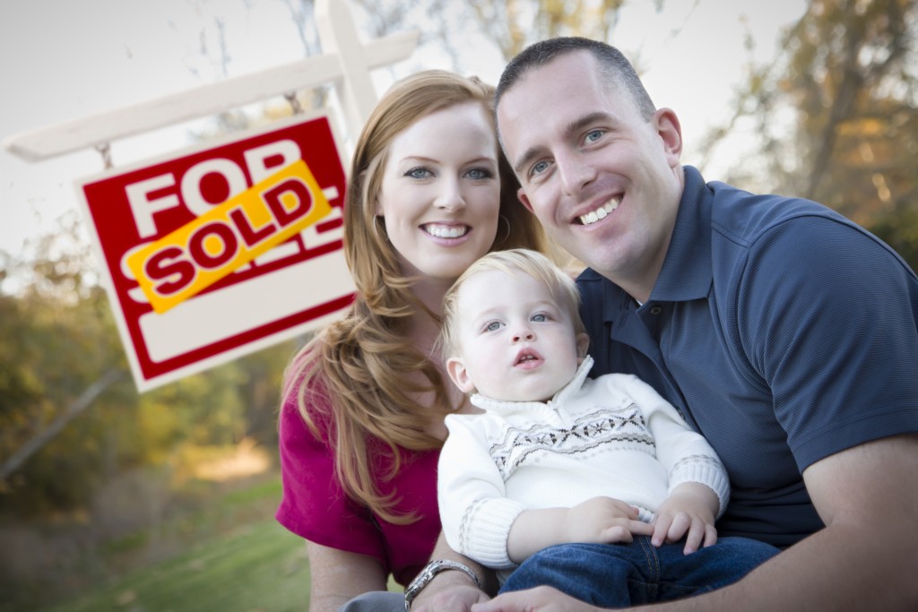 couple with baby in front of sold real estate sign