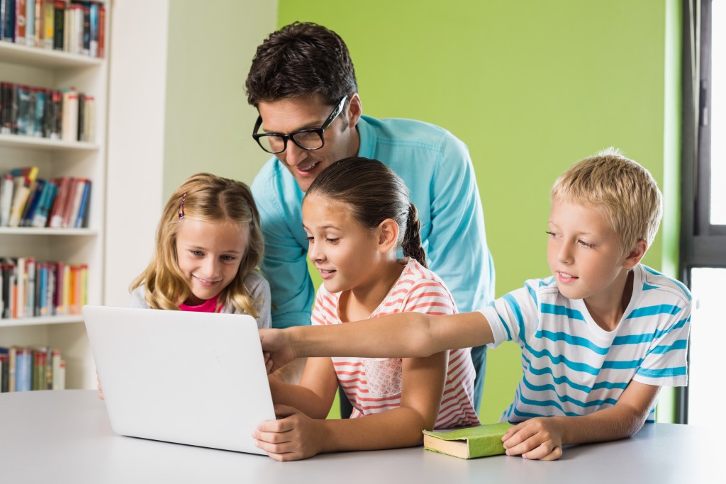 photo of three students in front of a laptop with their teacher