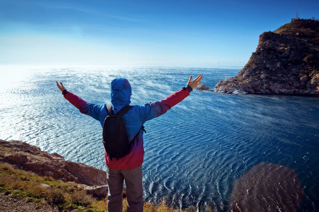 a man on top of the mountain raising his both hands in front of the sea